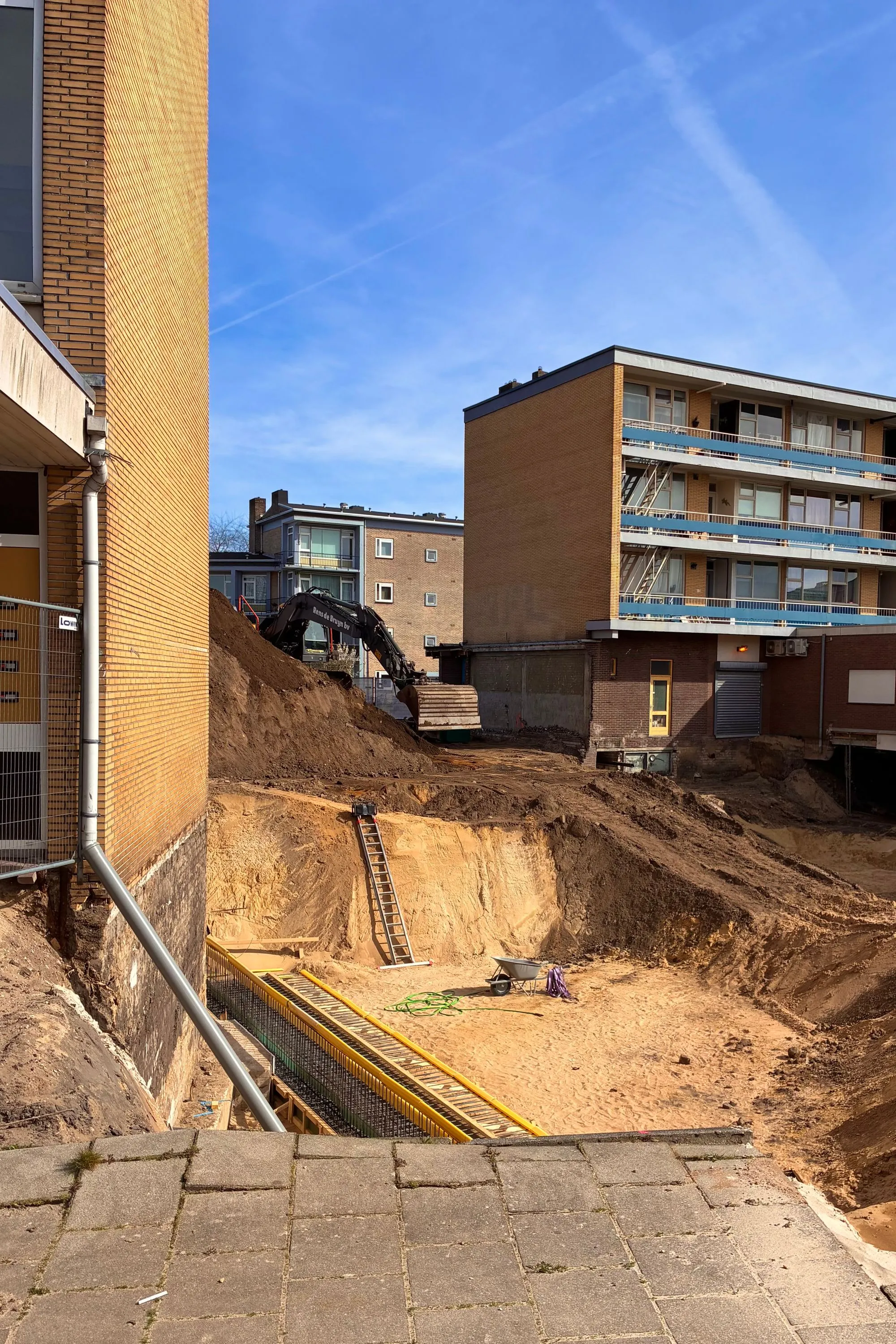 2026-03-20 - Big hole being dug by excavator between appartment buildings