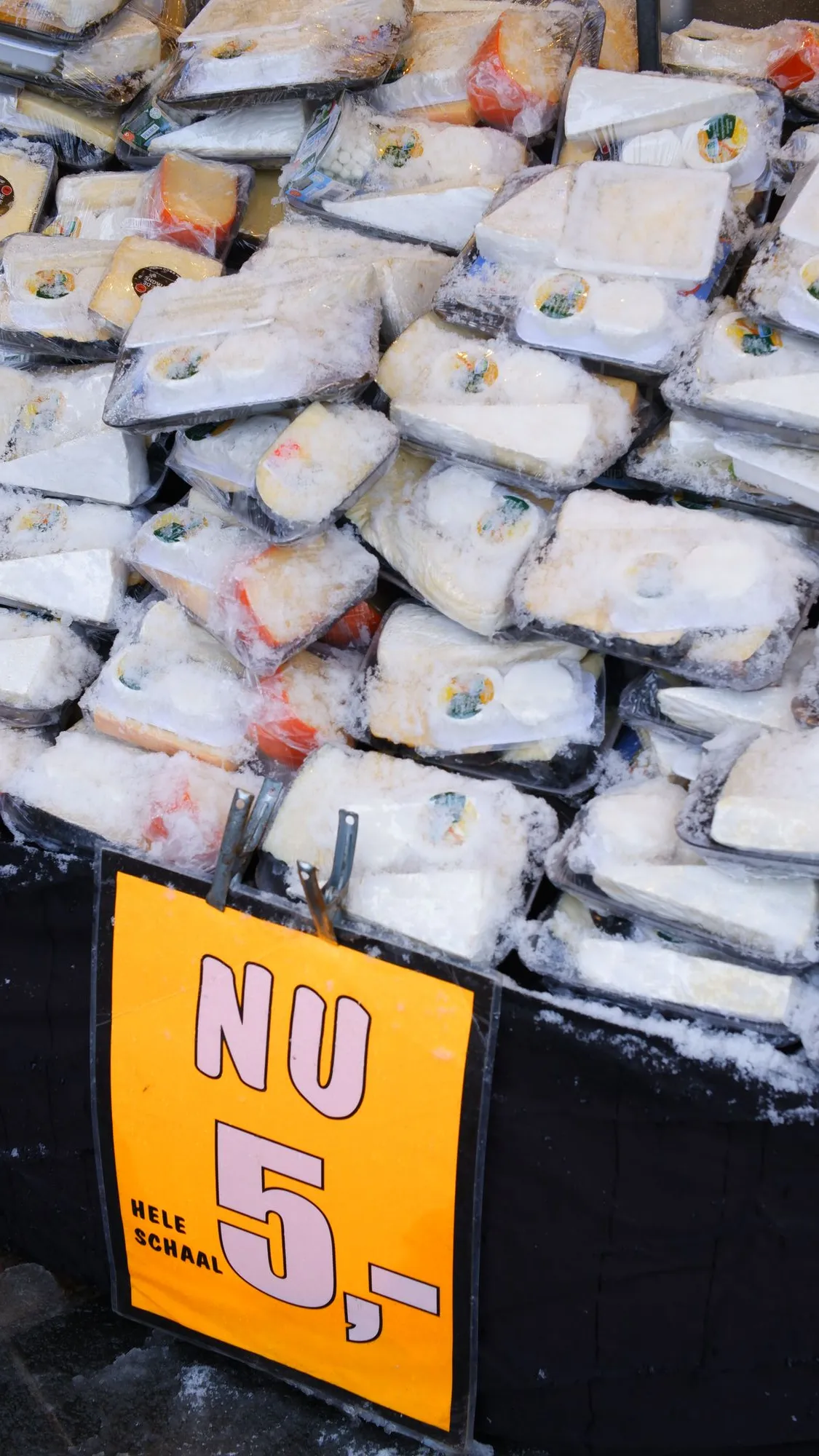 Cheese covered in snow with a sign that says "Nu 5,- Hele Schaal"