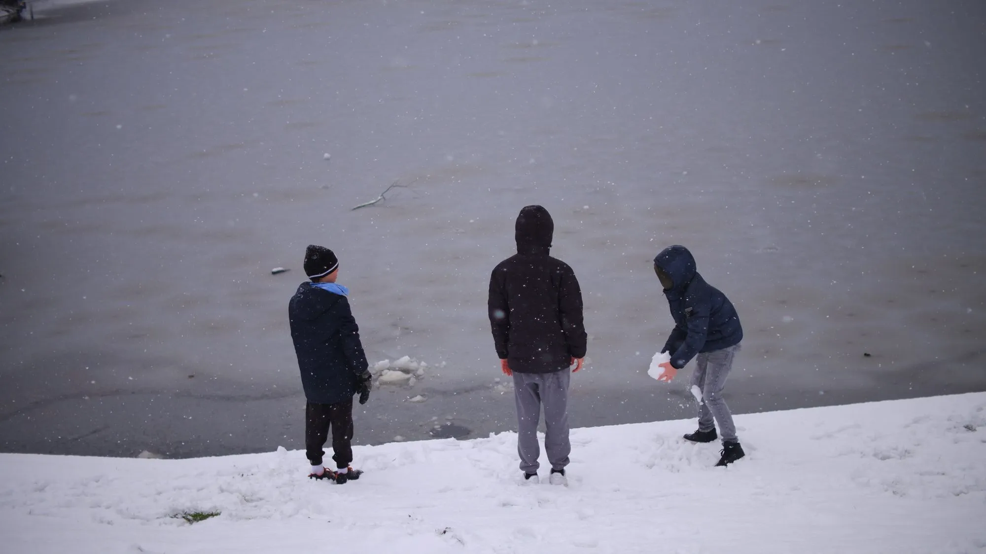 Kids throwing snow into the frozen lake