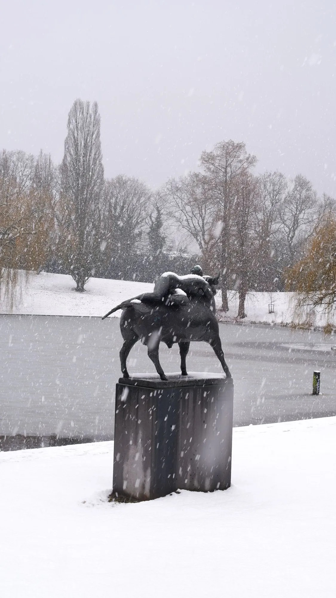 Statue of man riding bull in the middle of a snow storm