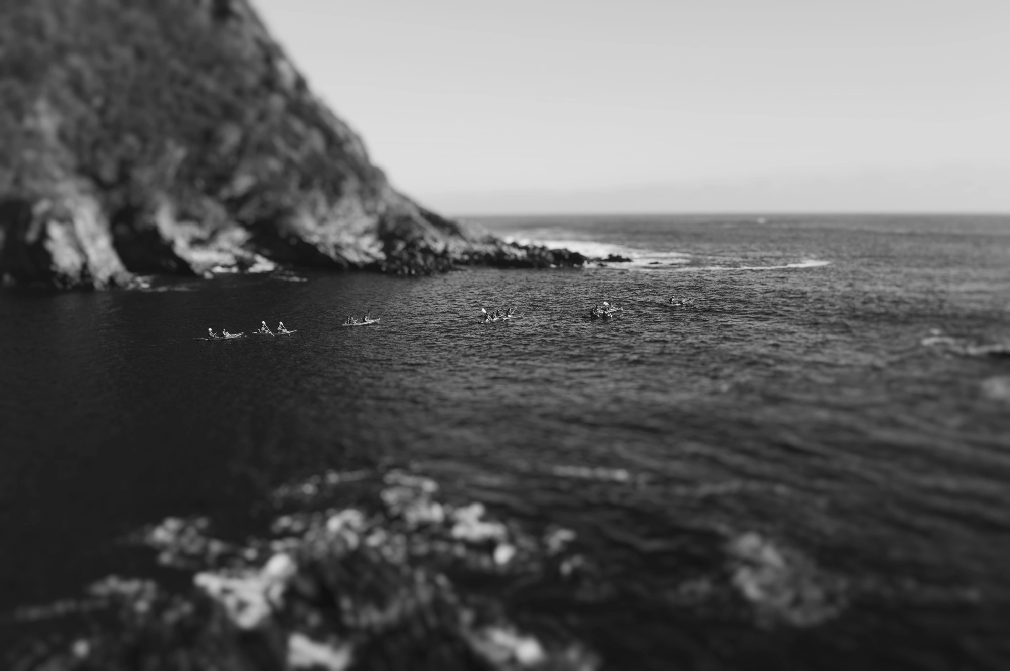 Kayaks in a row between mountains, rowing into the ocean