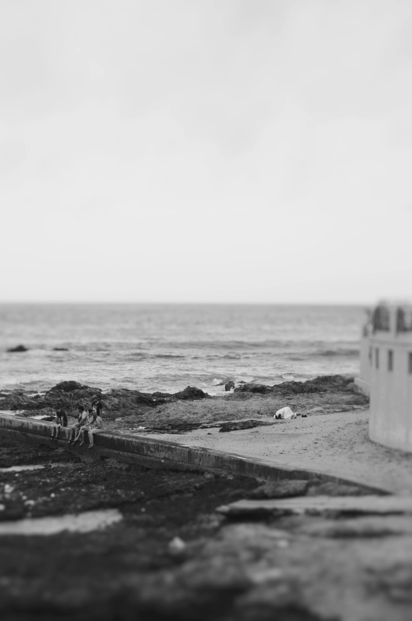 Man prays in distance with people sitting to the left next to the ocean