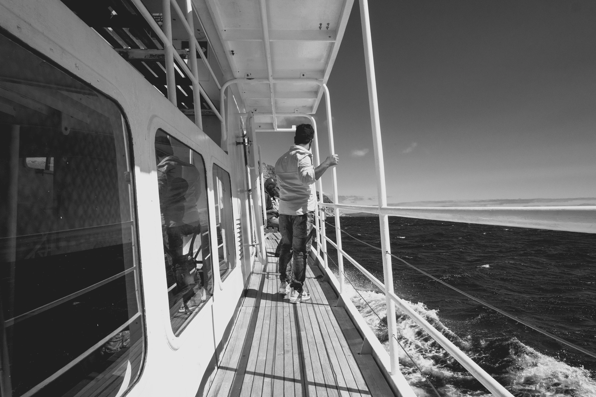 2022-02-13 - xt15-45 - bw - ZA - Cape Town - Man walks on walkway on boat beside the ocean