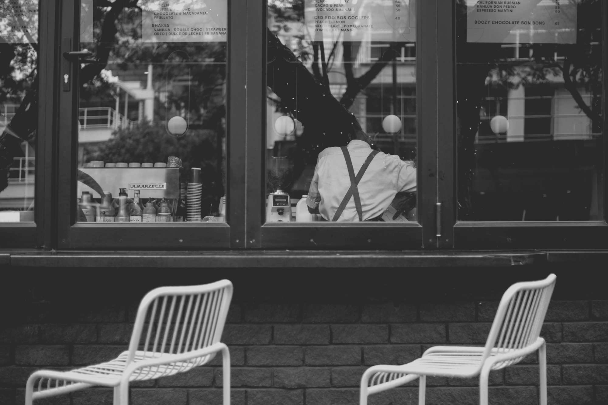 2021-12-19 - xt35 - bw - ZA - Rosebank, Johannesburg - Barrista working as seen through coffee shop window