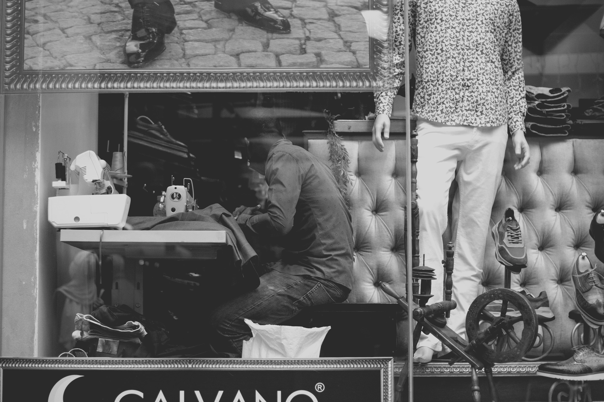 2021-12-19 - xt35 - bw - ZA - Rosebank, Johannesburg - Tailor working as seen through store window