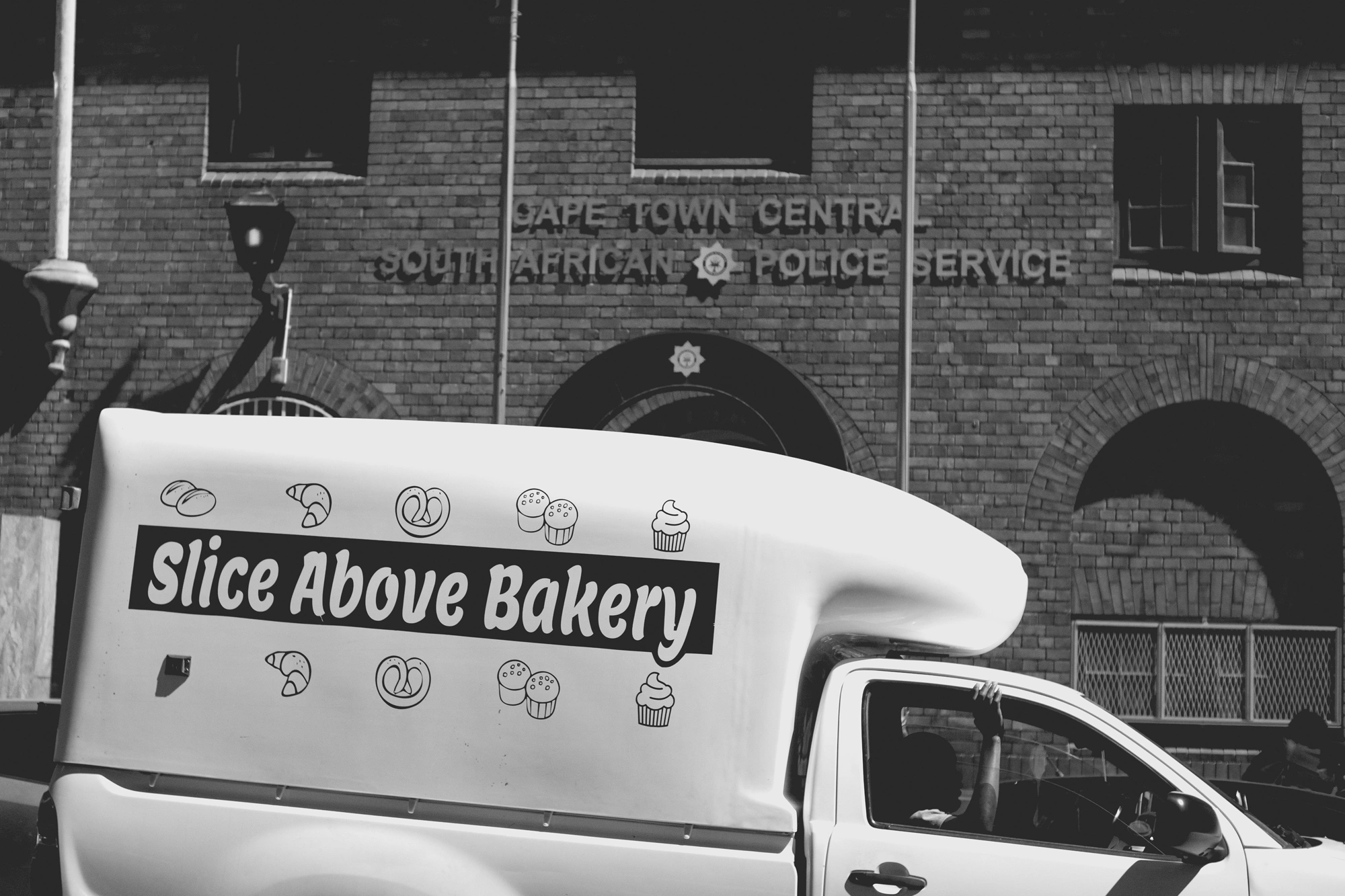 2022-02-17 - Cape Town - Man with arm out of window in a delivery van in front of a police building.j