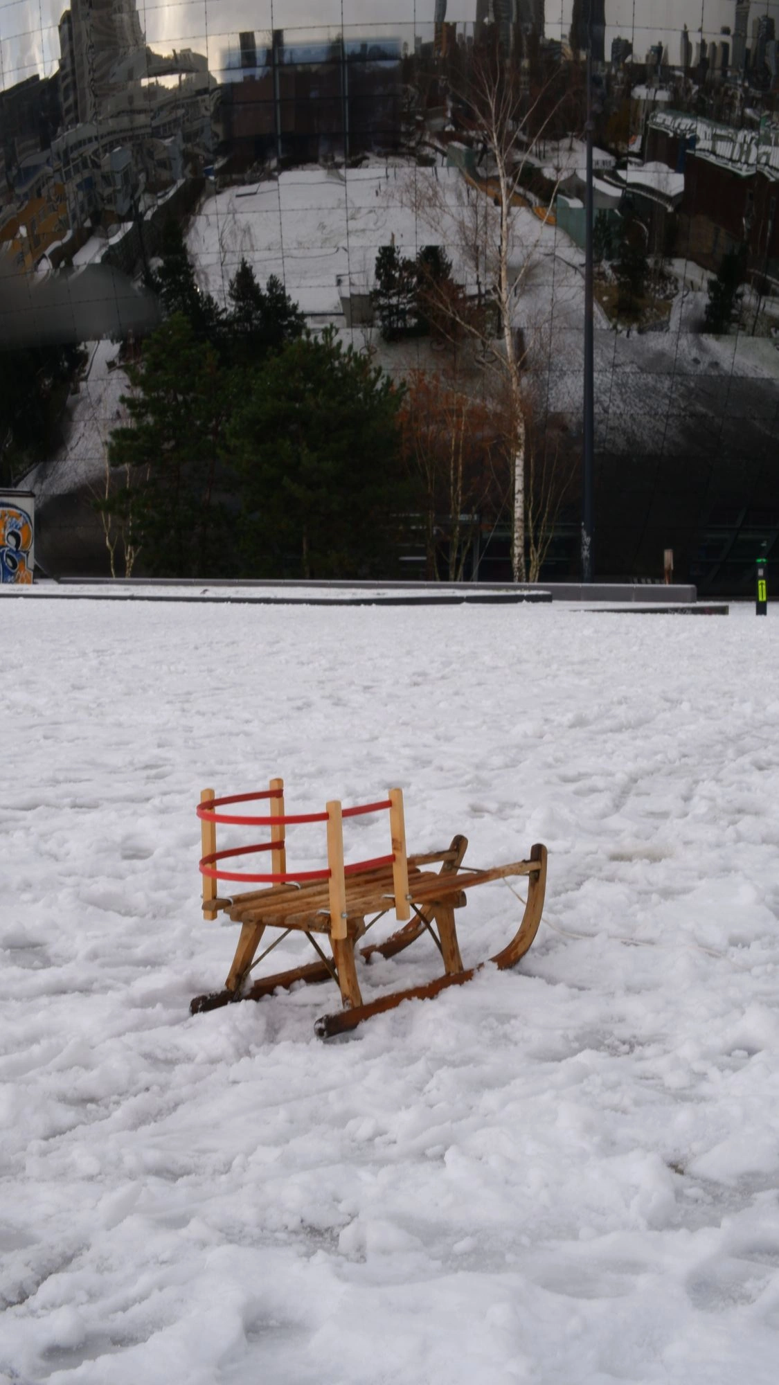 Sled on the snow in front of large mirror-covered building.J